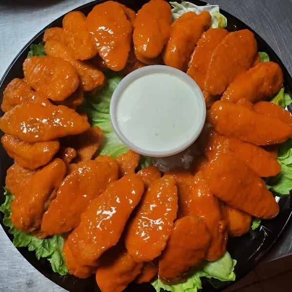 A platter of orange-glazed chicken wings arranged around a cup of white dipping sauce on lettuce.