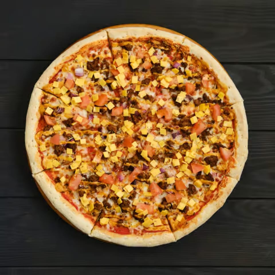 A whole pizza with ground meat, diced tomatoes, red onions, and cheese cubes on a dark surface.