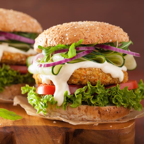 Two vegan burgers with lettuce, tomato, cucumber, red onion, and white sauce on a wooden board.